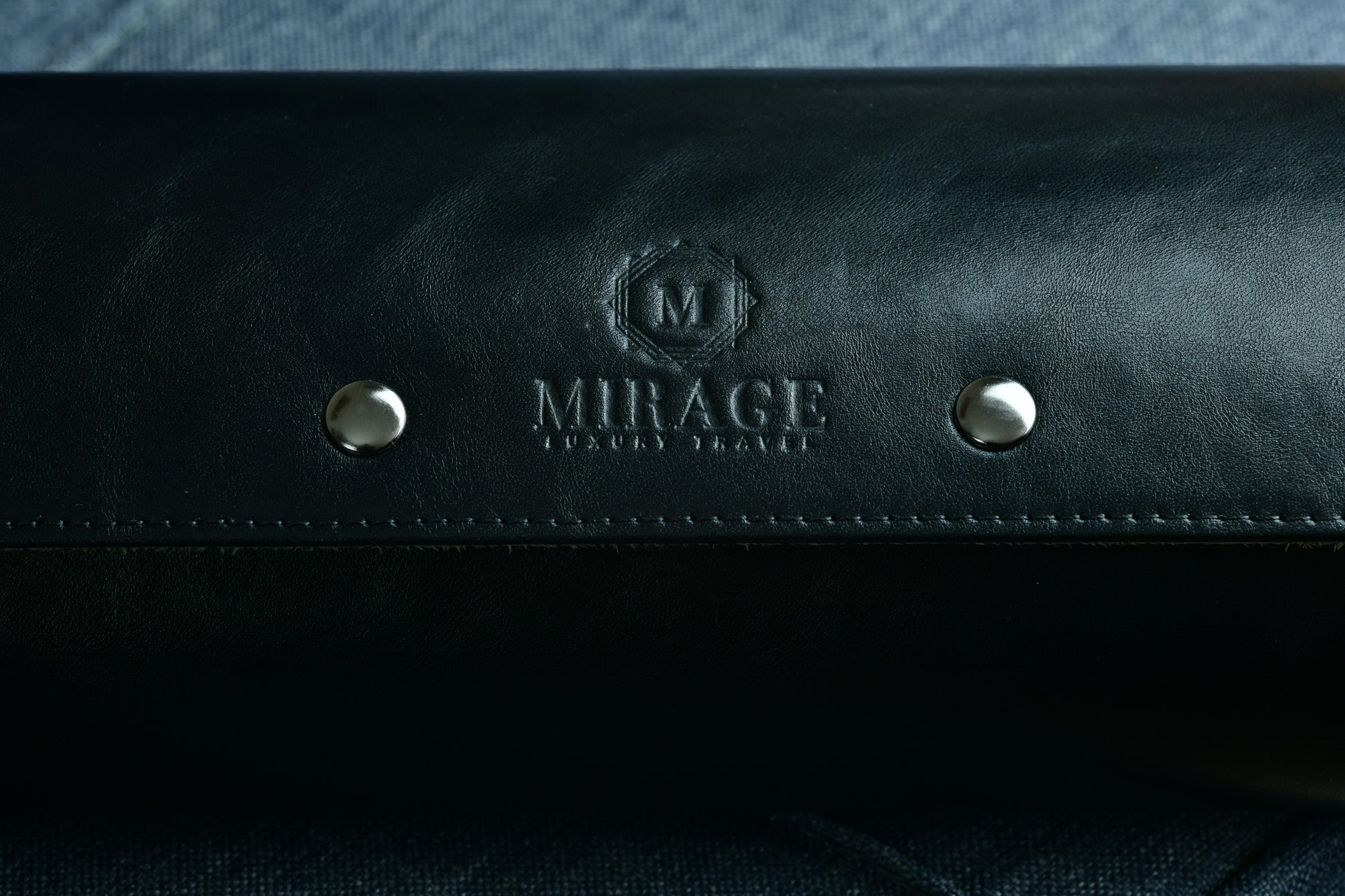 Close-up of the Mirage logo embossed on premium sable black Saffiano leather.